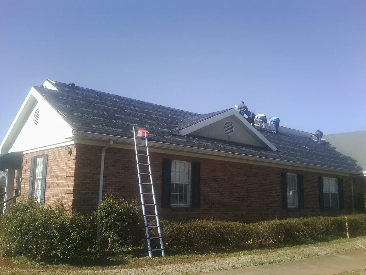 Crew tearing shingles off a brick ranch roof with a ladder set — Metal Roof Repair work by our crew in Markleysburg