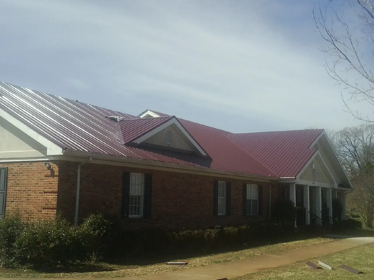Red metal roof with gabled entries on a long brick building, from a Hail Damage Roof Repair job in Markleysburg
