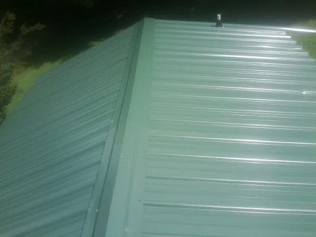 New green metal panels meeting at the ridge of a roof — Flat Roof Repair work by our crew in Markleysburg