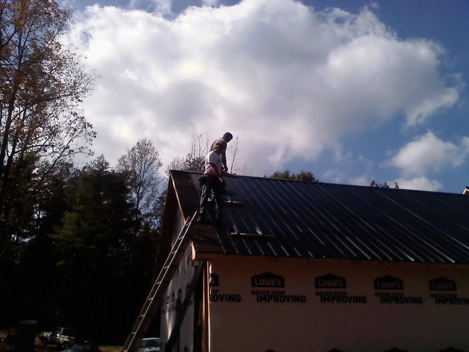 Roofer fastening dark metal panels high against a cloudy sky, from a Roof Inspection job in Markleysburg