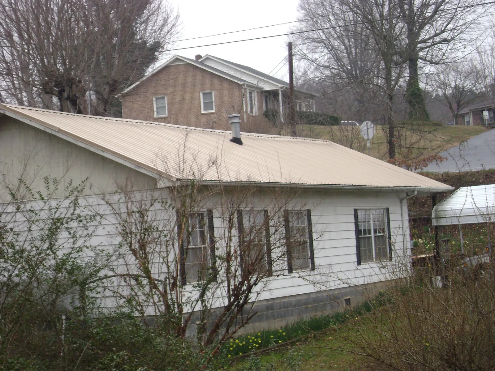 Tan metal roof on a white sided house set into a hillside — Commercial Roofing by Roofing Brothers in Markleysburg